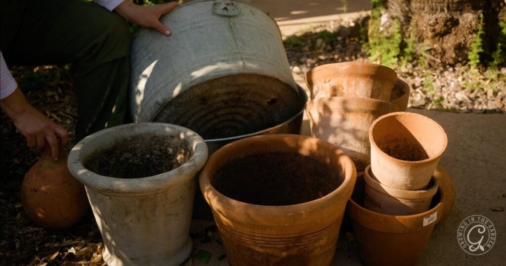 A person arranges empty clay and metal gardening pots outdoors on a sunny day, preparing for a hot climate summer garden.