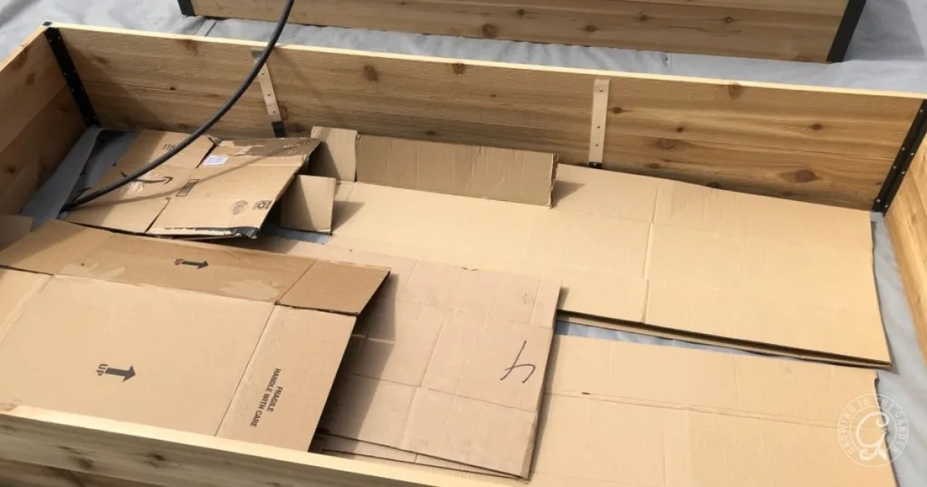 Wooden garden bed frame with flattened cardboard sheets laid inside it, showing an essential first step in How to Fill Raised Garden Beds.
